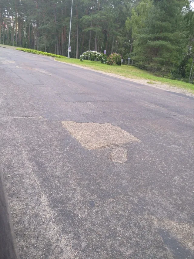 Large repaired asphalt patch surrounded by cracks on an approach road to Visaginas
