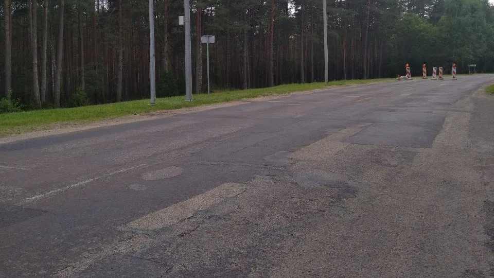 Patched and uneven asphalt with temporary roadwork barriers on an approach to Visaginas